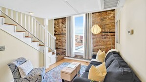 A living room with a staircase, a sofa, a chair, and a view through a large window. - The Vonkampen on Front! Perfect location in the Heart of Downtown! (wilmington)