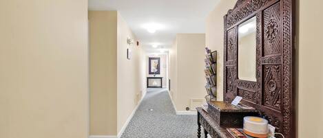 A hallway with a patterned carpet, a wooden console table with a mirror, and a framed picture on the wall.