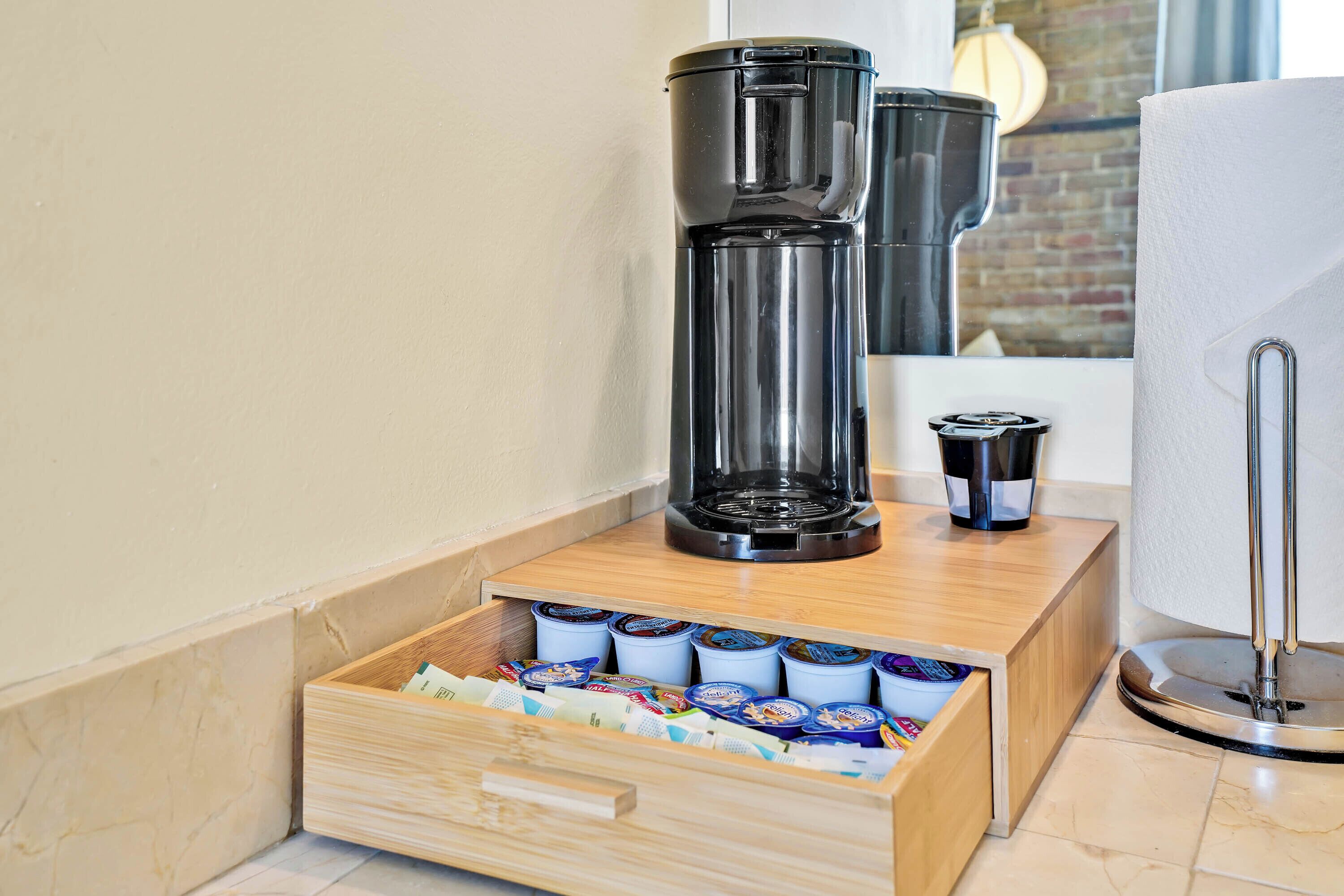 Een koffiehoek met een koffiezetapparaat, een lade vol koffiecups en een doos zakdoeken.