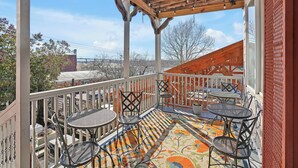 A covered outdoor patio with tables and chairs, a wooden ceiling with hanging lights, and a view of buildings and trees in the background. - The Vonkampen on Front! Perfect location in the Heart of Downtown! (wilmington)