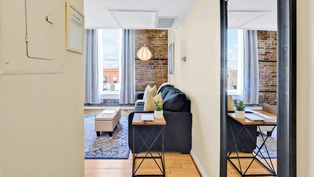 A modern living room with a black sofa, a wooden coffee table, and a brick wall. - The Vonkampen on Front! Perfect location in the Heart of Downtown! (wilmington)