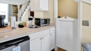 A compact kitchen with a sink, microwave, and a dish rack. A staircase is visible in the background leading to another room. - The Vonkampen on Front! Perfect location in the Heart of Downtown! (wilmington)