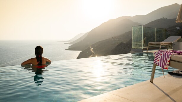 A person in a swimming pool with a view of the sea and mountains.