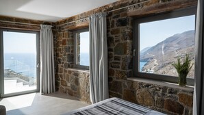 A room with stone walls, large windows, and a view of a coastal landscape.