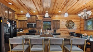 A rustic kitchen with wooden walls, a central island with bar stools, and a chandelier. - Heaven Sent - Sauna & Jacuzzi - Mini Golf (Broken Bow)