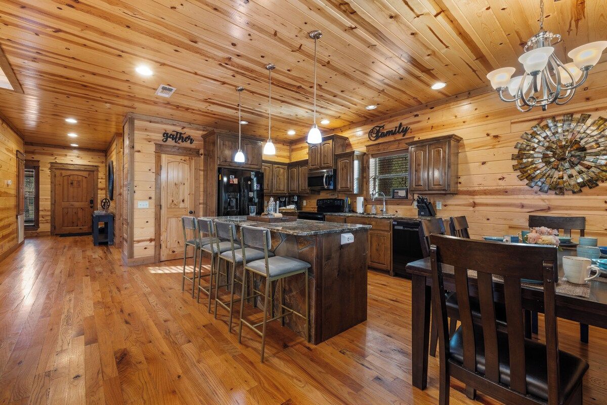 A wooden interior with a kitchen island, bar stools, and a chandelier.