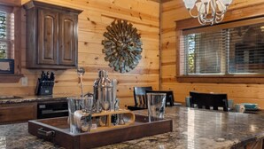 A kitchen with wooden walls, a granite countertop, a central island with glassware, and a decorative wall piece. - Heaven Sent - Sauna & Jacuzzi - Mini Golf (Broken Bow)