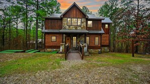 A two-story log cabin with a stone foundation, a front porch, and a gravel driveway. - Heaven Sent - Sauna & Jacuzzi - Mini Golf (Broken Bow)