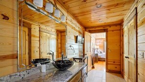 A wooden cabin interior with a kitchen featuring a marble countertop, a black bowl sink, and wooden cabinets. - Heaven Sent - Sauna & Jacuzzi - Mini Golf (Broken Bow)