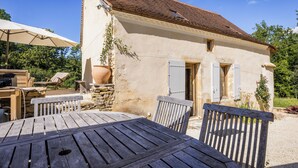 A rustic outdoor dining area with a wooden table and chairs, a stone wall, and a building with a tiled roof and shutters. - Exceptional PIGEONNIER in Périgord (Saint-Germain-des-Prés)
