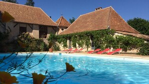 A swimming pool with red lounge chairs and a building with tiled roofs. - Exceptional PIGEONNIER in Périgord (Saint-Germain-des-Prés)