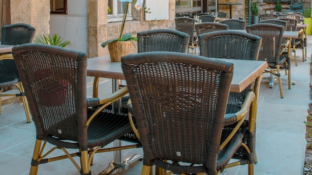 An outdoor seating area with wicker chairs and tables, a stone building with a 'HOTEL' sign, and a tower in the background. - Hotel du Roy (Aisey-sur-Seine)
