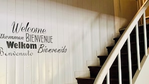 A staircase with a white banister and a wall with a 'Welcome' sign in multiple languages. - Hotel du Roy (Aisey-sur-Seine)