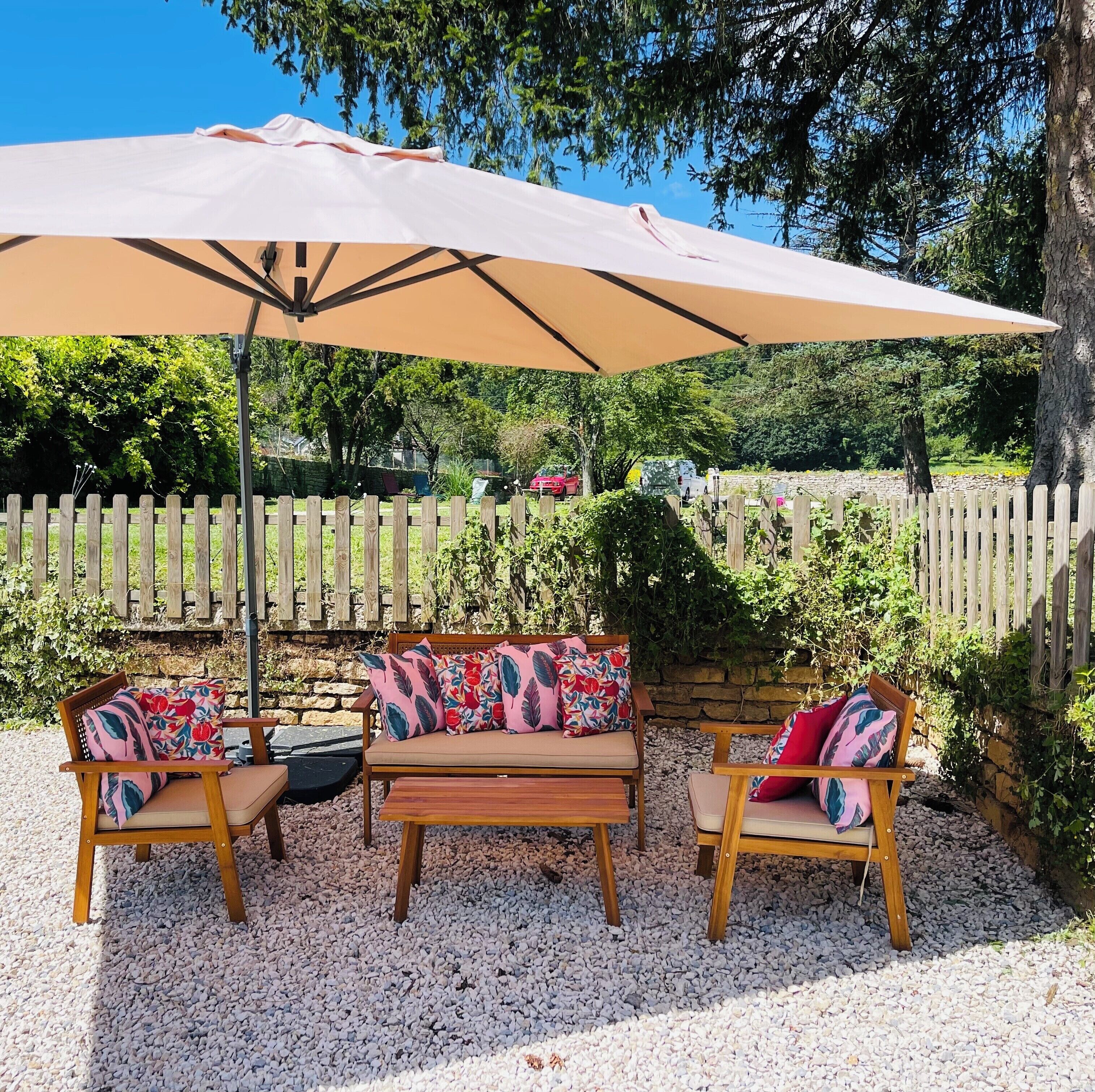 An outdoor seating area with a wooden bench and a table, covered by a large umbrella.