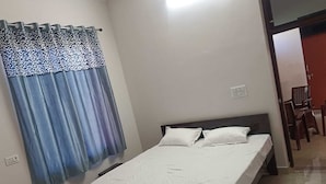 A single bed with a dark headboard and white bedding in a room with a blue curtain.