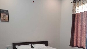 A bedroom with a single bed, a nightstand, a water bottle, and a window with curtains.