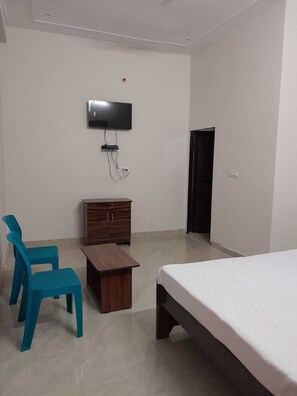A bedroom with a bed, a TV mounted on the wall, a wooden cabinet, and a small table. - Riya Home Stay (Sawai Madhopur)