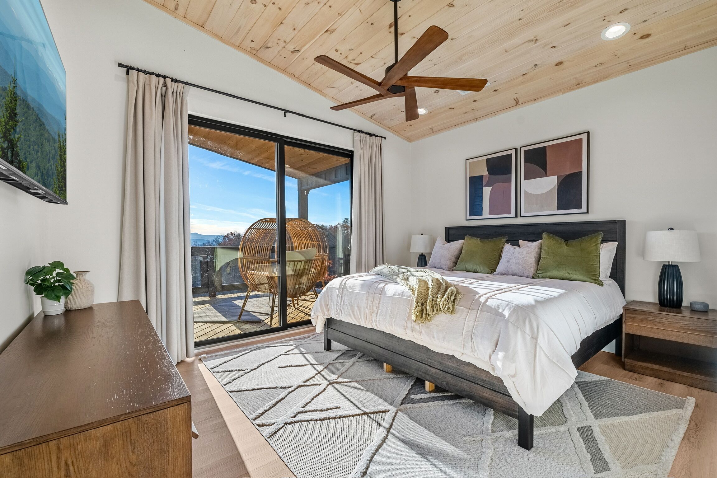 A bedroom with a bed, a ceiling fan, a large window, and a view of the outdoors.