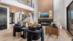 A spacious living area with a fireplace, a balcony, and a large TV screen. - Stunning View, Modern Cabin in Gatlinburg, Htd Indoor Pool, Hot Tub, Game Room! (Gatlinburg)