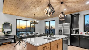 A modern kitchen with a central island, stainless steel appliances, and large windows offering a view of the outdoors. - Stunning View, Modern Cabin in Gatlinburg, Htd Indoor Pool, Hot Tub, Game Room! (Gatlinburg)