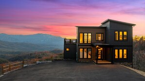 A modern two-story house with large windows, a covered driveway, and a view of mountains. - Stunning View, Modern Cabin in Gatlinburg, Htd Indoor Pool, Hot Tub, Game Room! (Gatlinburg)