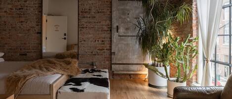 A cozy room with a brick wall, a large mirror, a wooden bench, a leather sofa, and a potted plant.