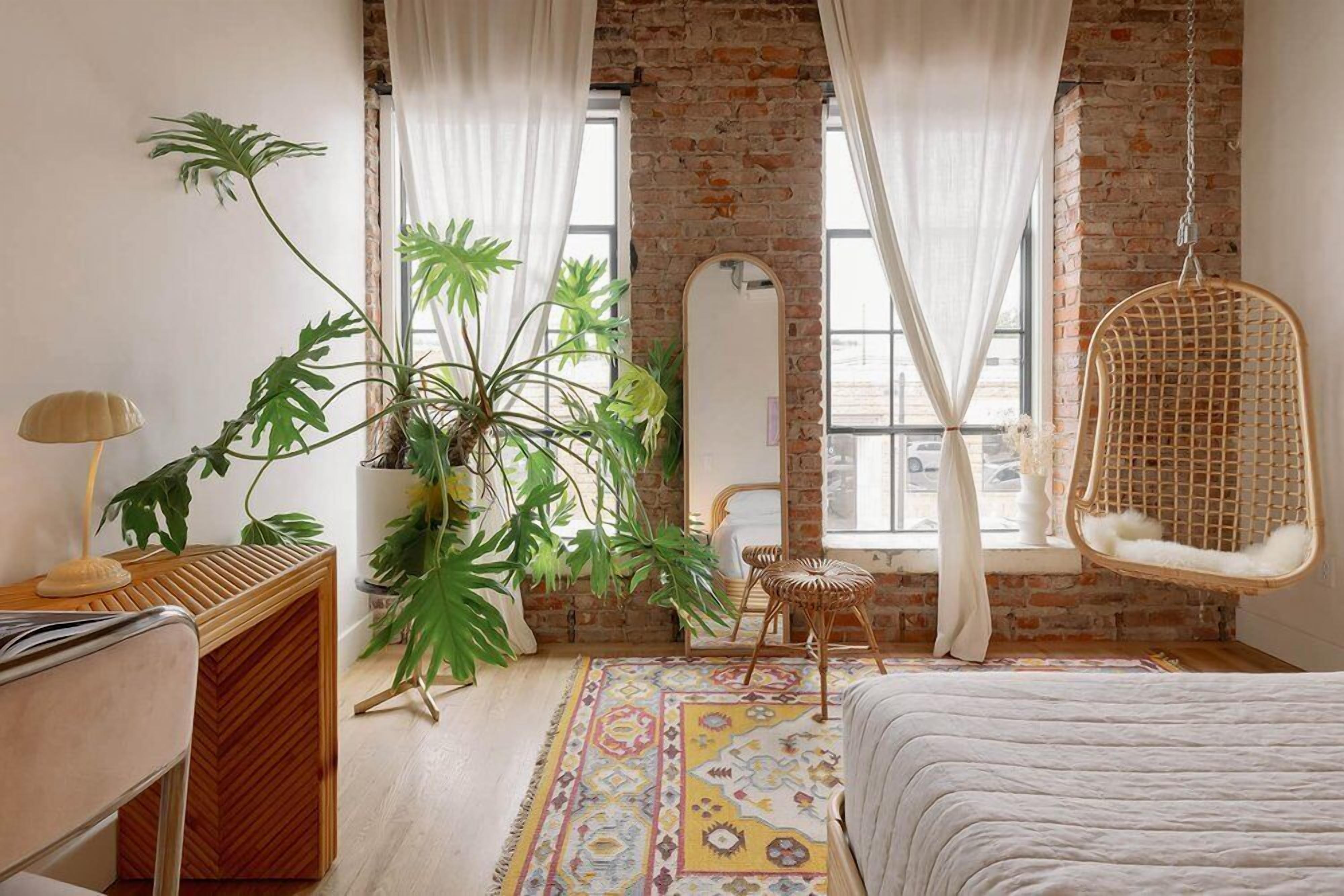 Un dormitorio con pared de ladrillo, una silla colgante, una planta grande y un tapiz estampado.