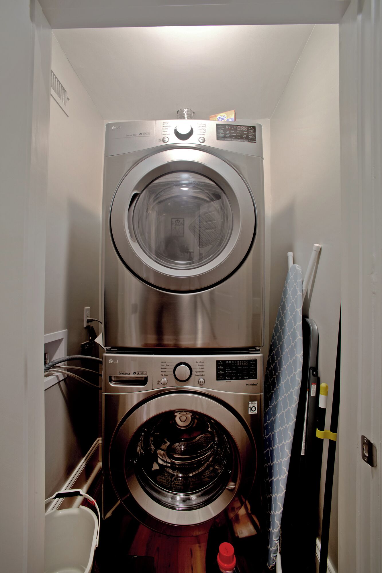 Un appareil combiné lave-linge et sèche-linge, compact et en acier inoxydable, à chargement frontal, installé dans un couloir étroit.