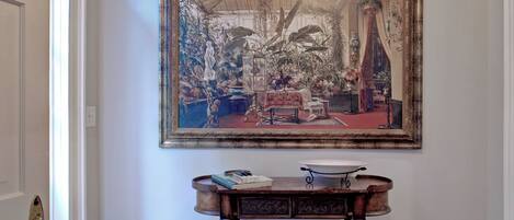 A hallway with a wooden floor, a white door, and a large framed painting on the wall.
