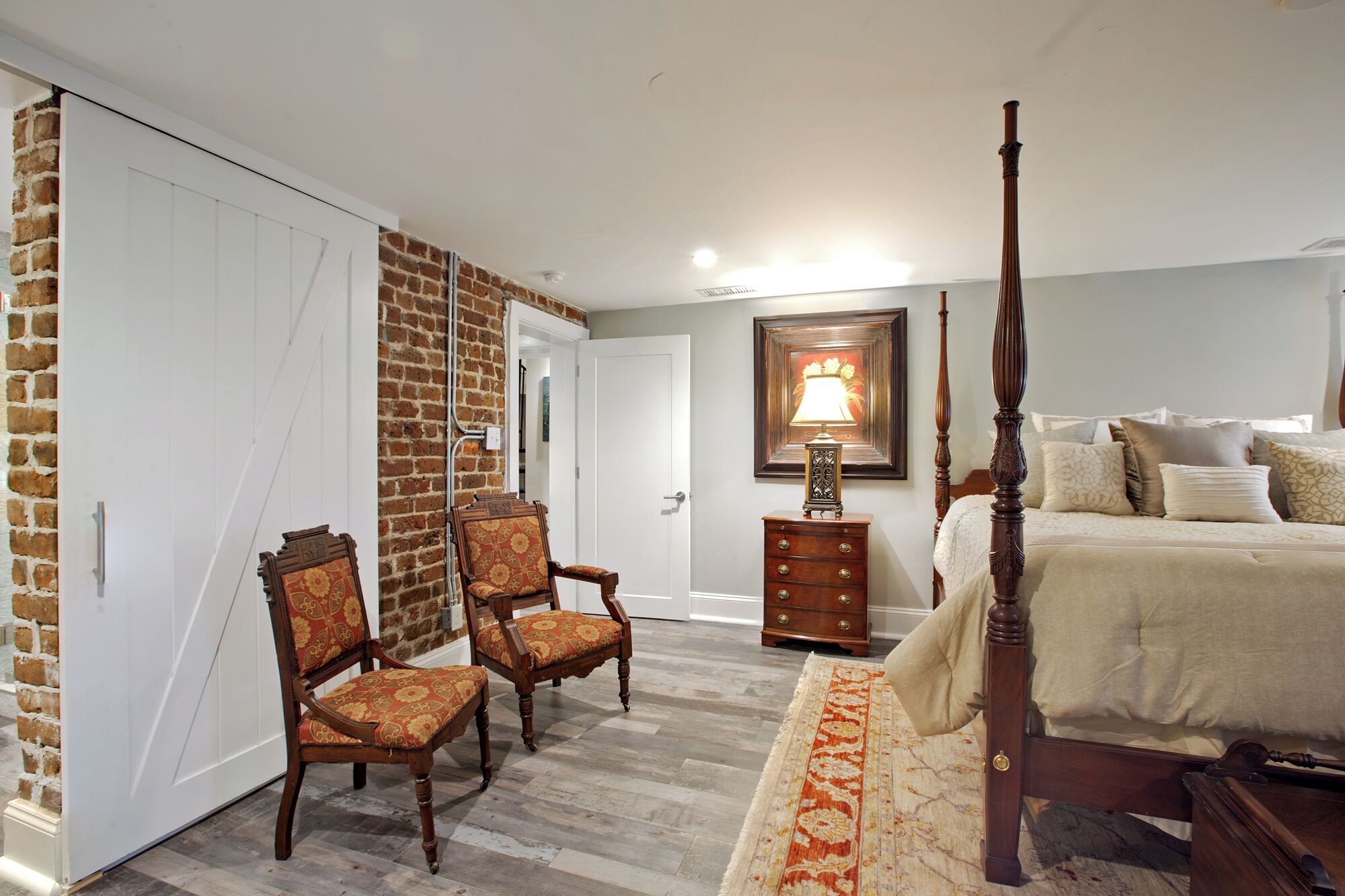 Quarto com uma cama de dossel, duas poltronas estofadas, uma mesa de cabeceira de madeira, um aparador e um tapete estampado.