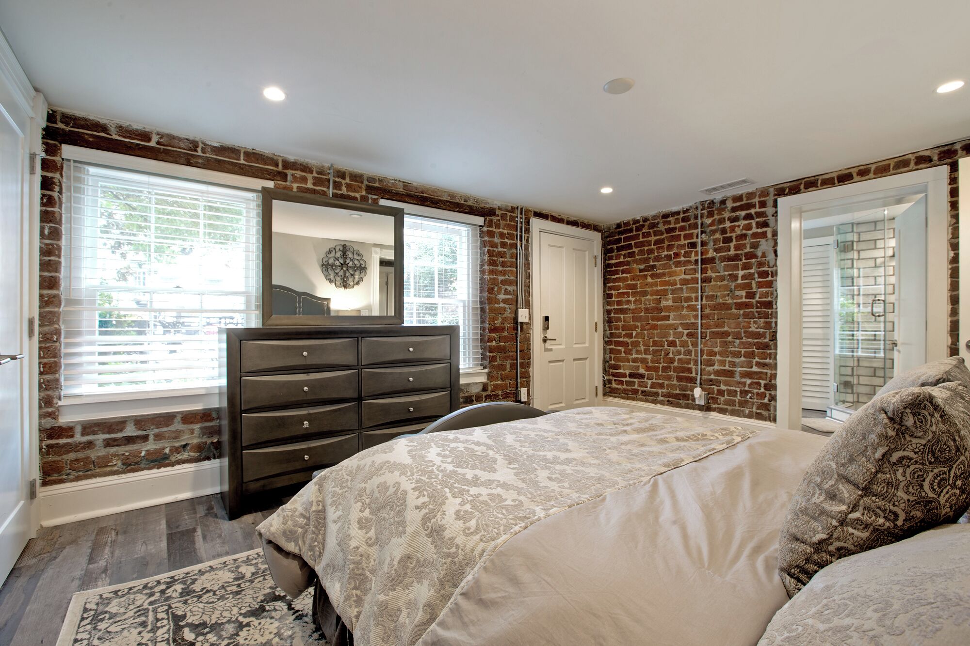 Een slaapkamer met een bakstenen muur, een dressoir, een bed met beddengoed met dessin, en een raam met zonwering.