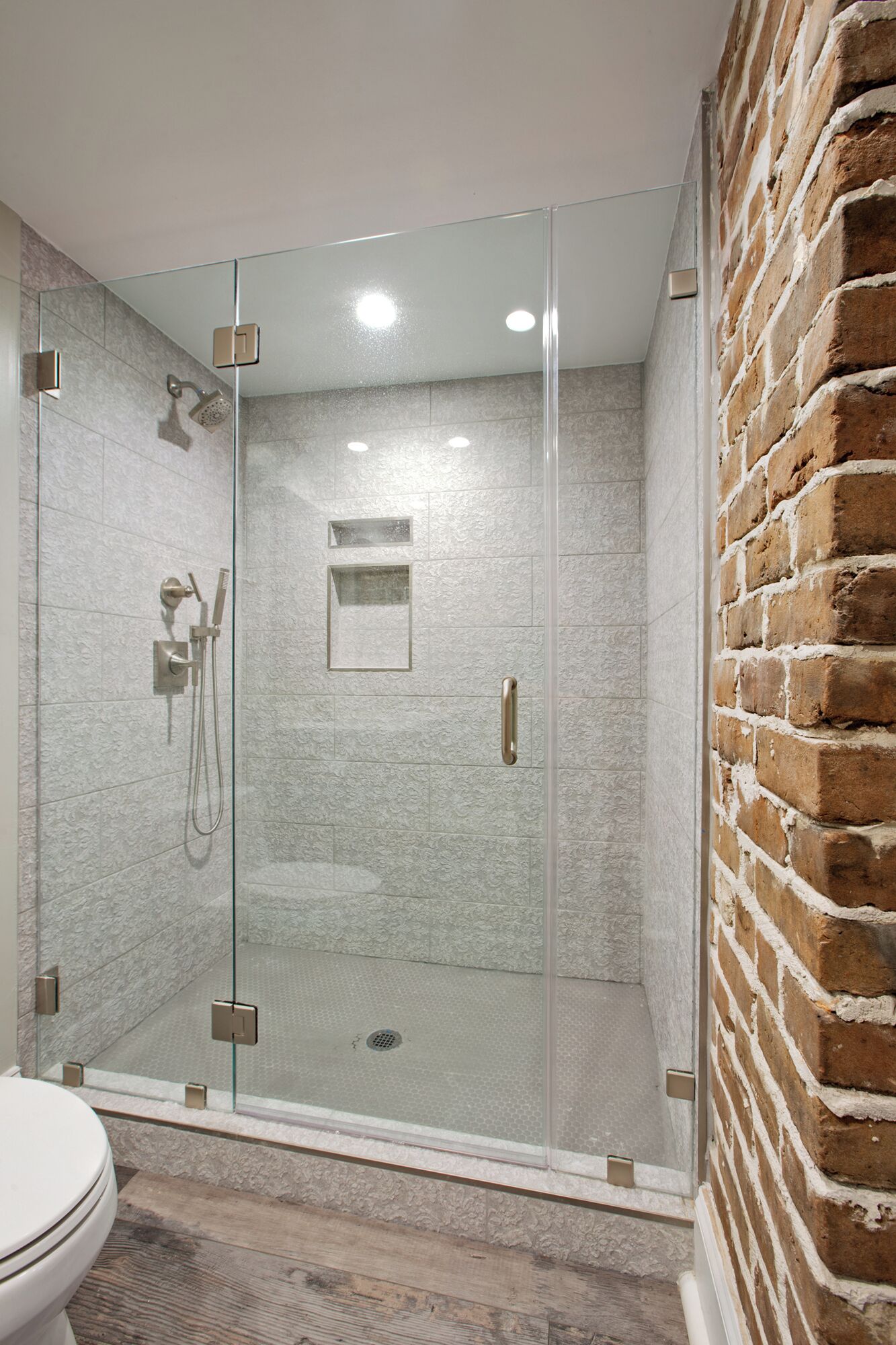 A modern bathroom with a glass-enclosed shower, a white toilet, and a brick wall.