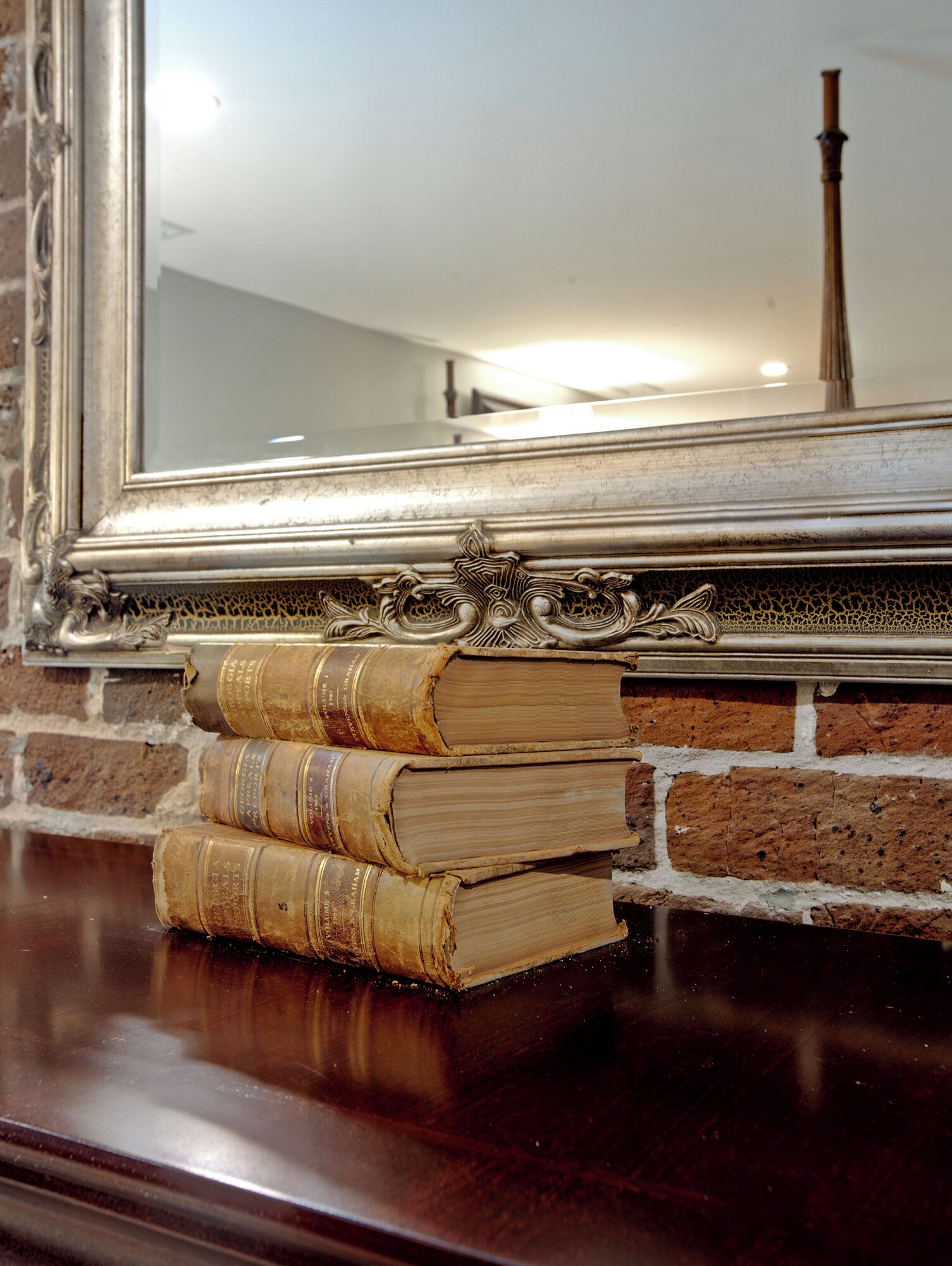 Une pile de vieux livres posée sur une surface en bois, avec un miroir qui reflète un mur en briques et un objet en bois.