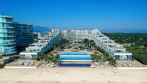 A resort with multiple swimming pools, a beach, and a mountainous backdrop. - Luxury Beachfront Apartment with Infinity Swimming Pools in Nuevo Vallarta (Nuevo Vallarta)