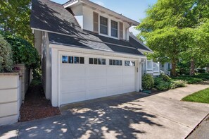 A residential garage with a white door, a sloped roof, and a driveway leading to a house.