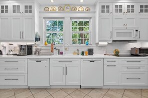A modern kitchen with white cabinetry, a double sink, and a window with a view of trees.
