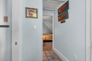 Een smalle gang met een bed op de achtergrond, een ingelijst schilderij aan de muur en een plafondlamp.
