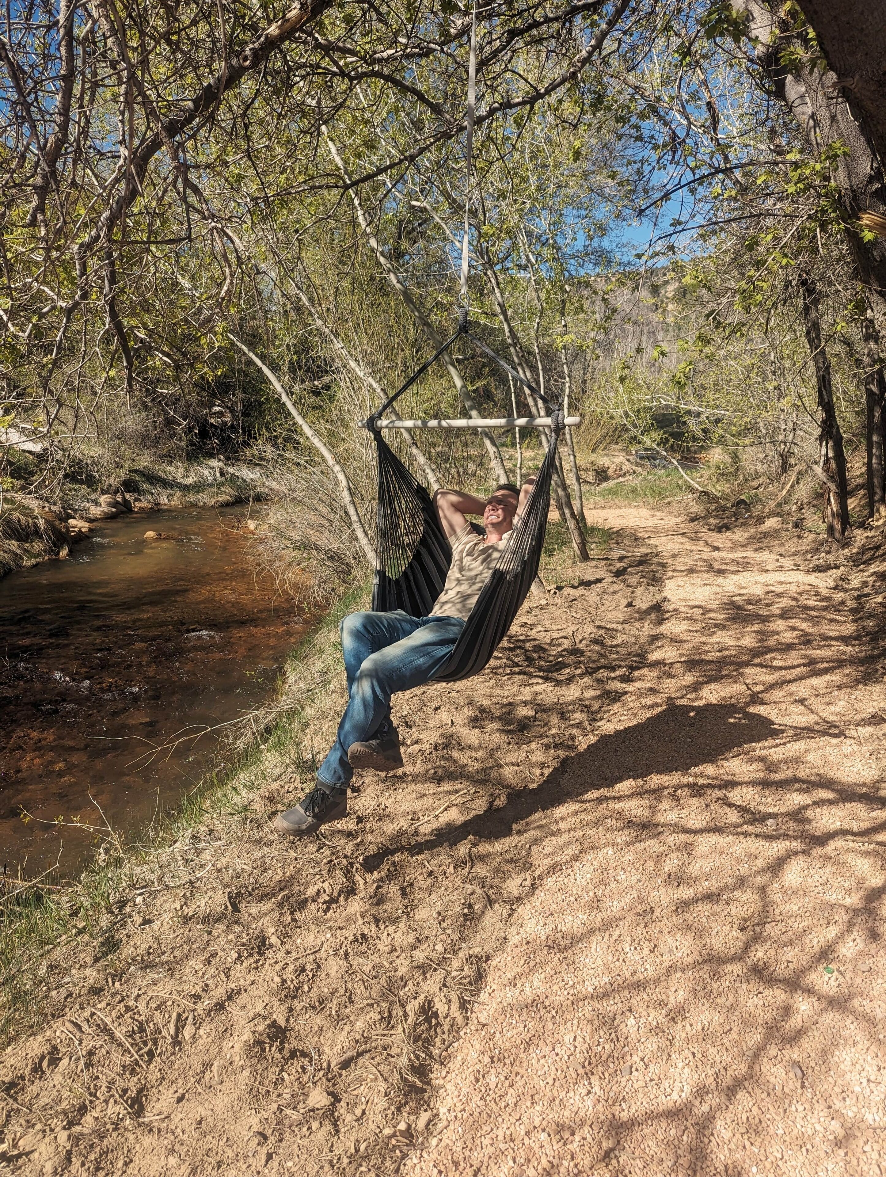 Un hamac suspendu entre des arbres, dans un cadre naturel, avec un ruisseau à proximité.