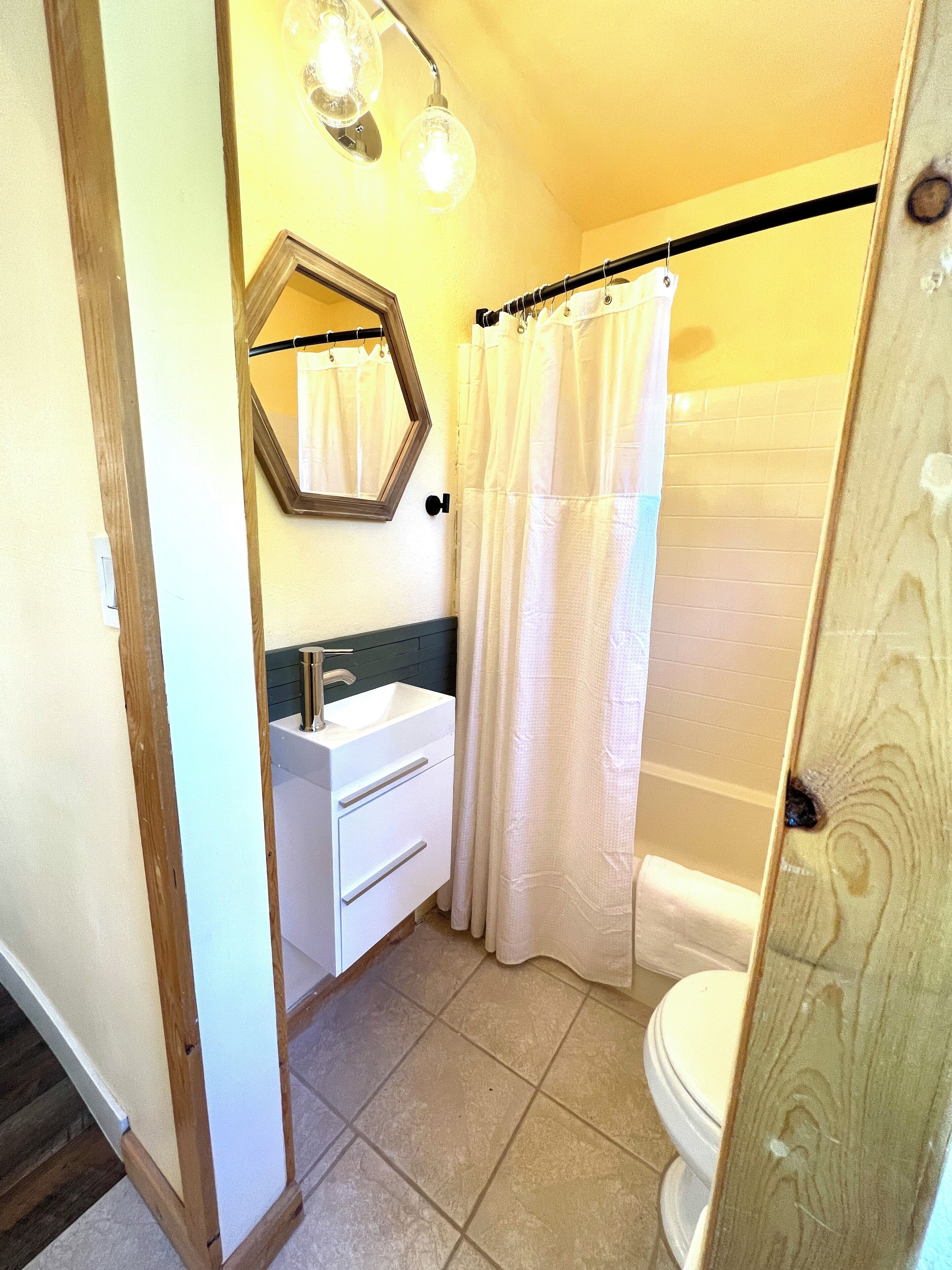 Une salle de bain avec un lavabo blanc, un miroir et un rideau de douche.