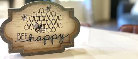 A wooden sign with a honeycomb design and bees, placed on a table in a room with a blurred background.
