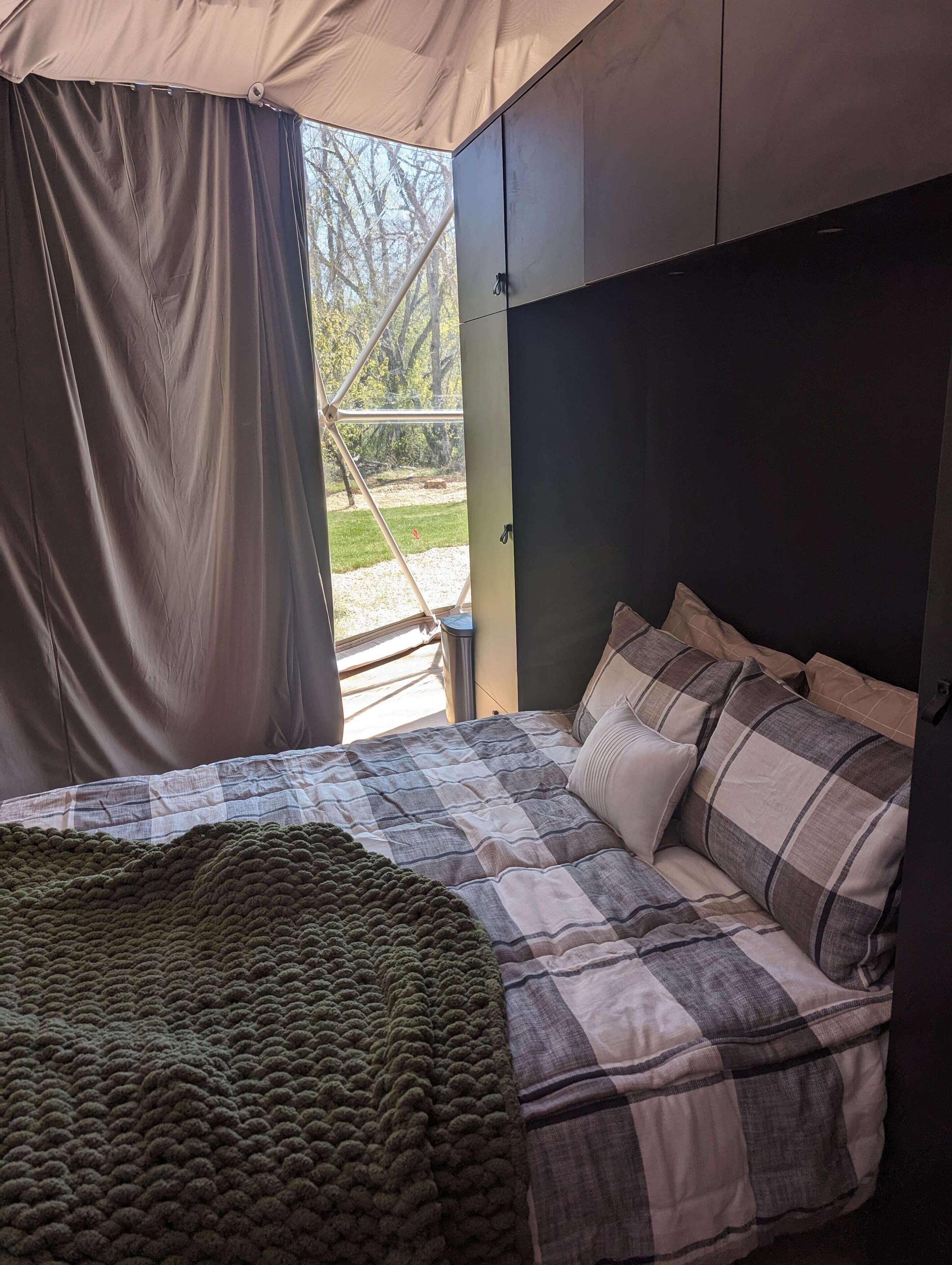 Een tentkamer met een bed, een groen gebreide deken en een geruit sprei.