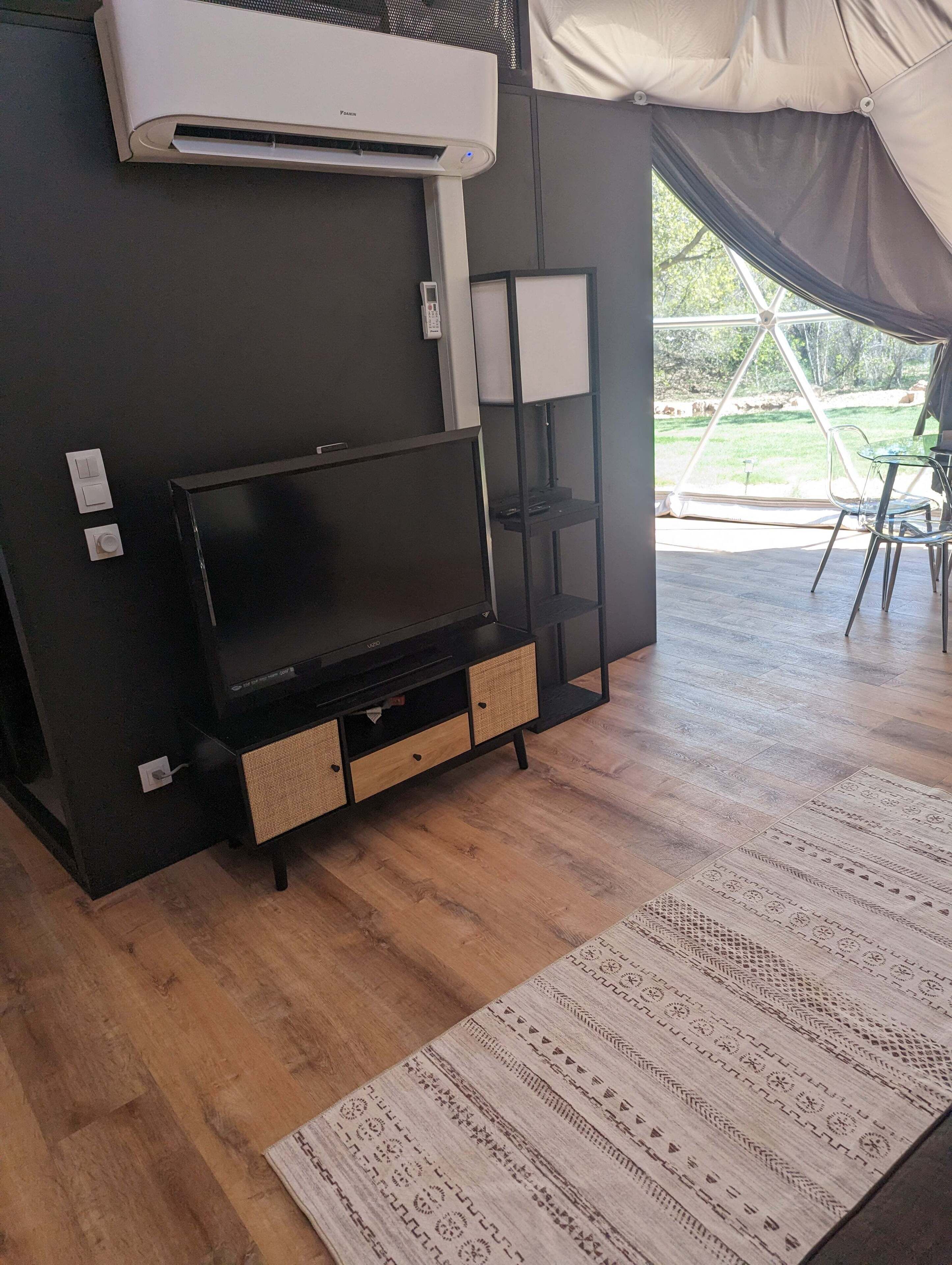 Un soggiorno moderno con TV a schermo piatto, condizionatore integrato e un'ampia finestra con vista sull'esterno.