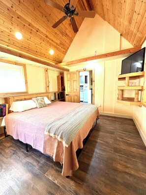 A bedroom with a bed, wooden ceiling, and a television on a wooden stand.