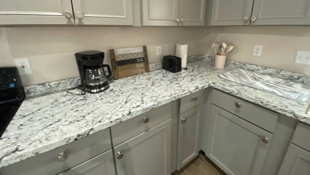 A kitchen with light grey cabinets, a marble countertop, a coffee maker, a box labeled 'but first coffee', and a container with utensils. - Fabulous 3-bedroom house with AC in Cleveland (Cleveland)