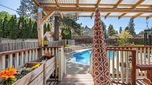 A wooden deck with a pool, surrounded by a wooden fence and a pergola with a metal roof. - Poolside Getaway with Spacious Outdoor Living & 6 Cozy Beds!! (Spokane)