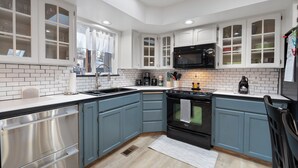 A modern kitchen with white cabinetry, a black microwave, stainless steel appliances, and a large window. - Poolside Getaway with Spacious Outdoor Living & 6 Cozy Beds!! (Spokane)