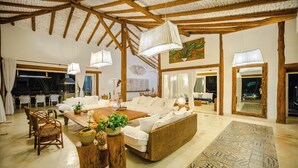 A spacious living room with a large sofa, wooden coffee table, and wicker chairs. There are hanging lights and a patterned rug on the floor. - Casa Mandala Corumbau (Corumbau)