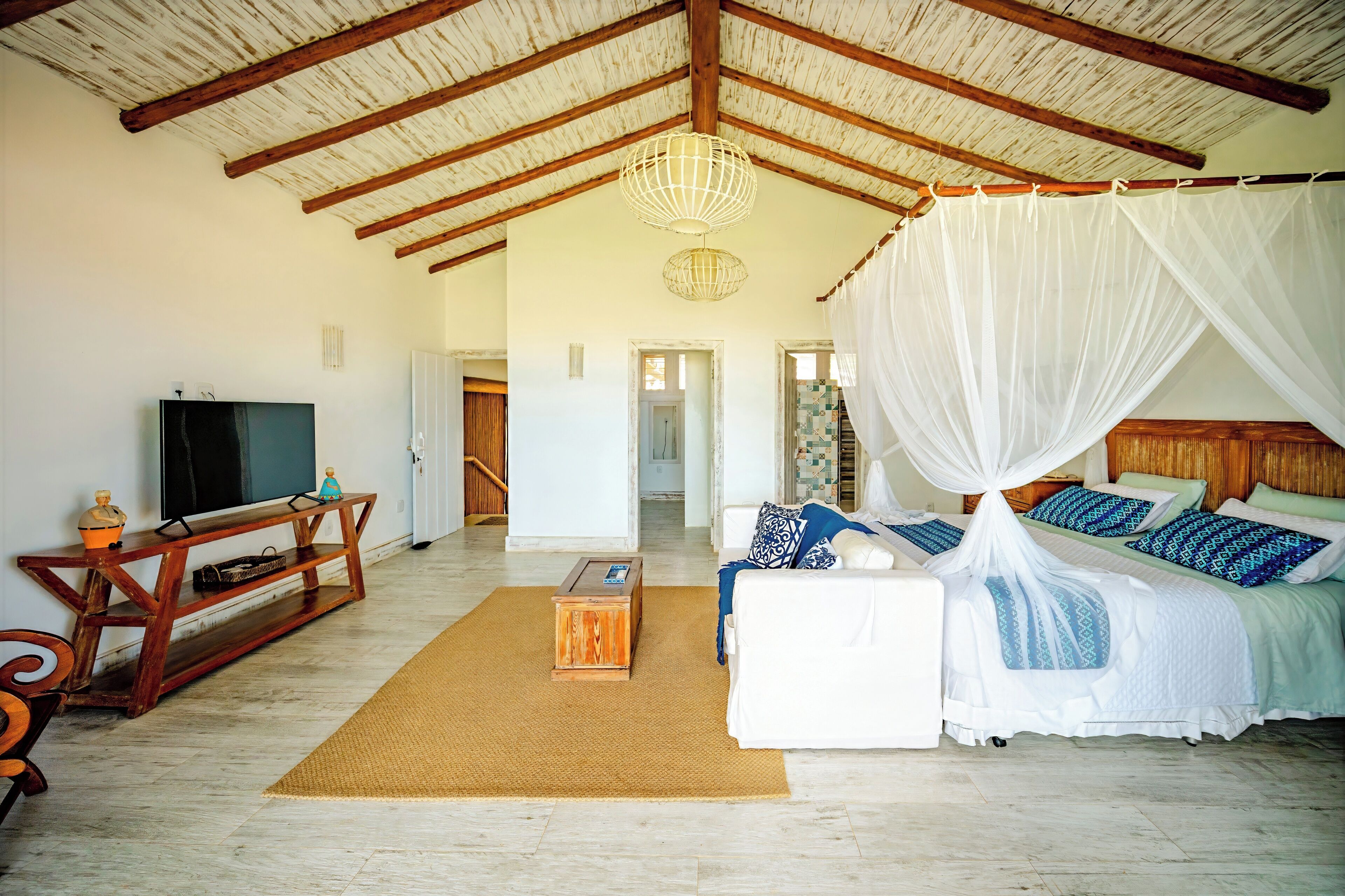 A spacious room with a high ceiling, a bed with a canopy, a television, and a wooden console table.