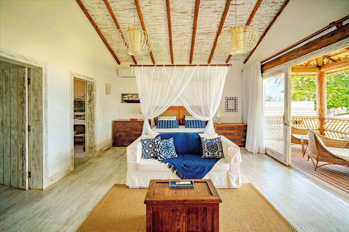 A bedroom with a canopy bed, wooden flooring, and a view of the outdoors.