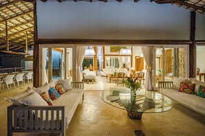 A spacious living area with a glass coffee table, white sofas, and a view of the outdoor patio. - Casa Mandala Corumbau (Corumbau)
